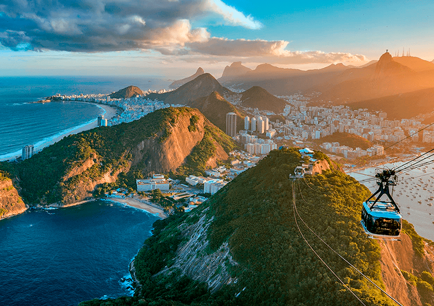 Vista aérea do Pão de Açúcar no Rio de Janeiro ao pôr do sol, com bondinho, orla e montanhas.