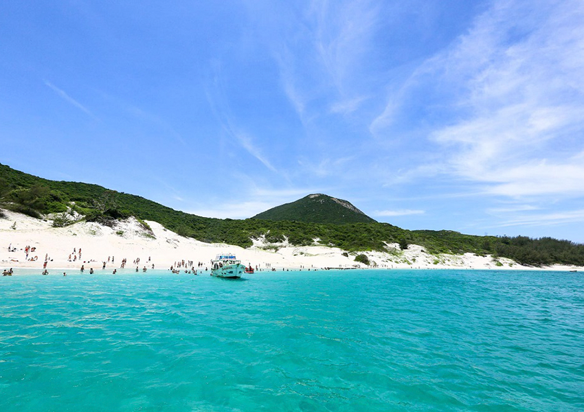 Praia do Farol em Arraial do Cabo, com faixa de areia branca, vegetação nativa e água turquesa.