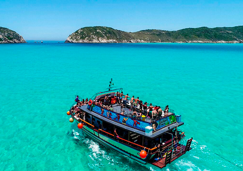 Escuna de passeio com turistas navegando nas águas cristalinas de Arraial do Cabo, Rio de Janeiro.